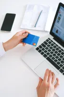 A person looking at their credit card while using their laptop